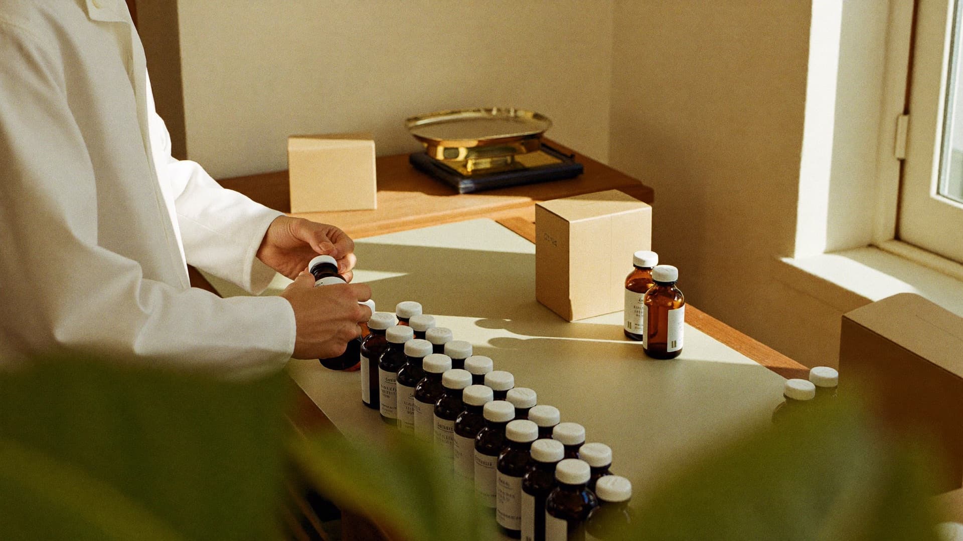 Hands arranging amber bottles on a warm pharmacy workbench