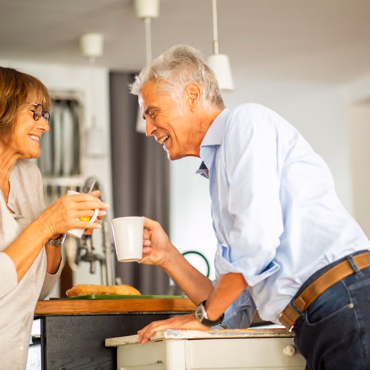 An older couple laughing together over morning coffee in their kitchen