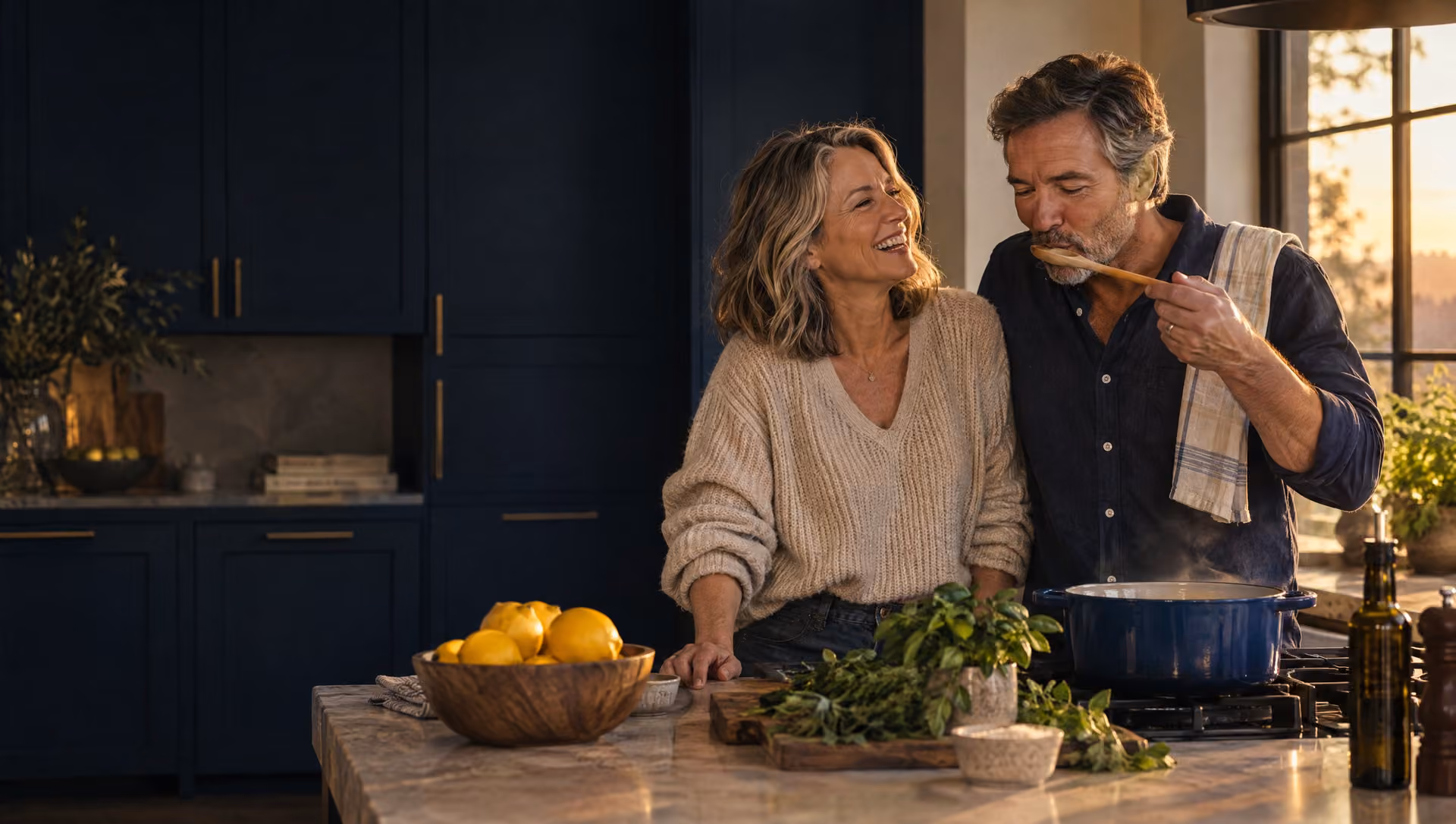 A couple in their fifties cooking together in a navy kitchen in evening light